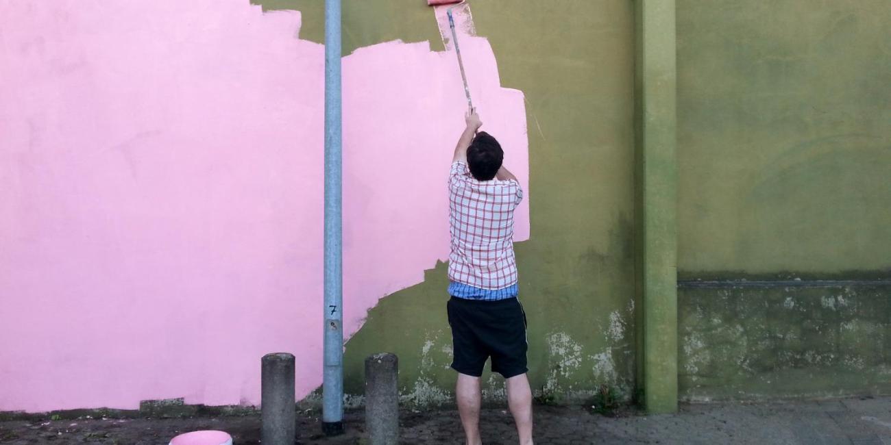 Ein Mann streicht eine graue Wand mit rosa Farbe an.