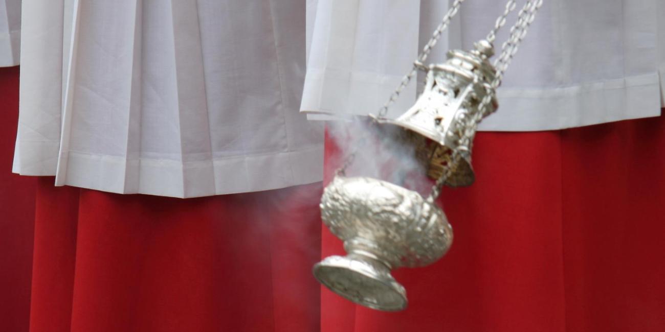 Weihrauchfass in der Hand eines Ministranten, rote und weiße Gewänder im Hintergrund.