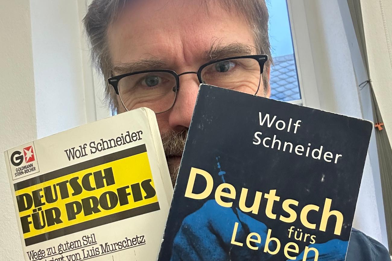 Ein Mann hält zwei Bücher in die Höhe