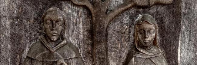 Holzrelief mit zwei stehenden Figuren unter einem Baum, eine mit Kind, eine mit Schleier.
