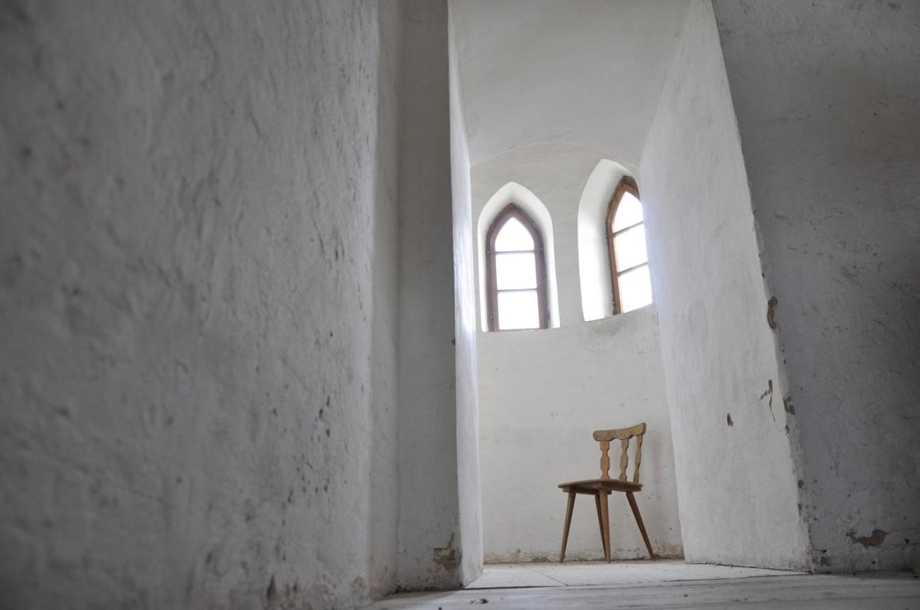 Ein einzelner Stuhl steht in eines Ecke  einer Kirche unter zwei Fenstern.