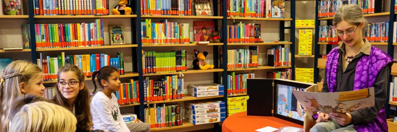 Eine Frau liest Kinder in einer Bücherei aus einem Buch vor