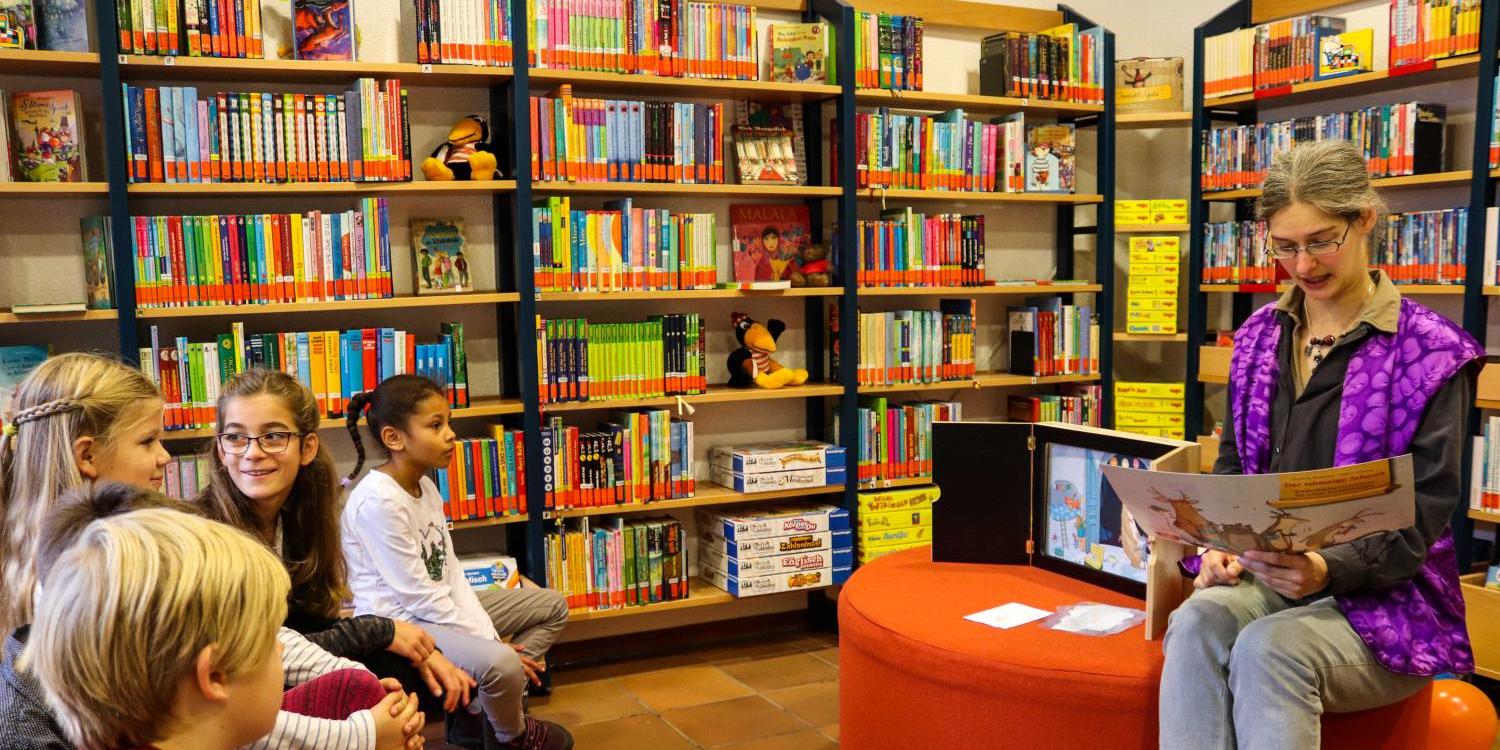 Eine Frau liest Kinder in einer Bücherei aus einem Buch vor