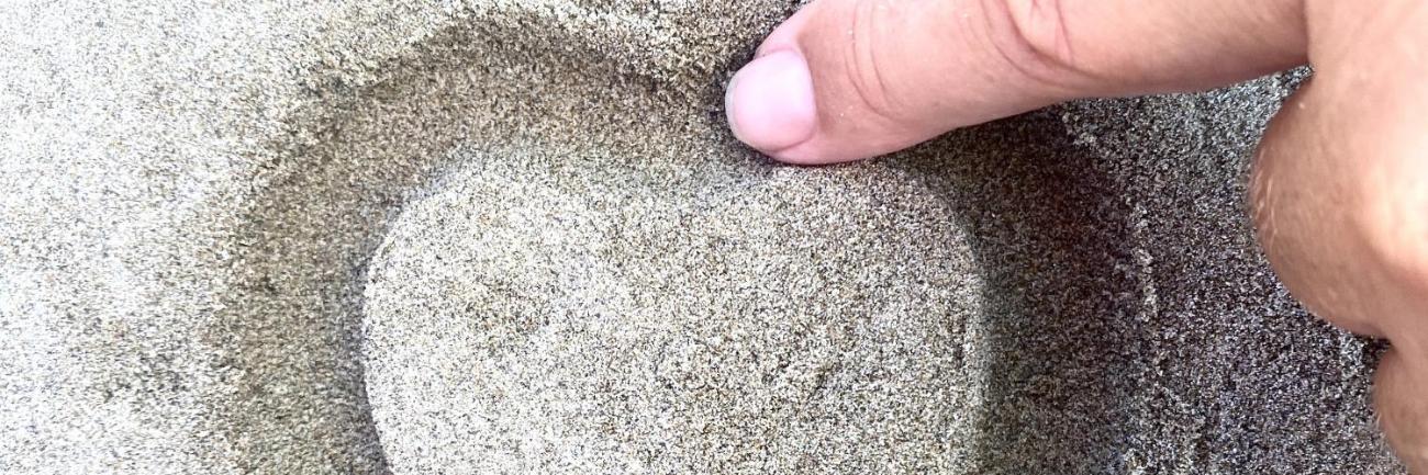 Ein Finger zeichnet ein Herz in den Sand