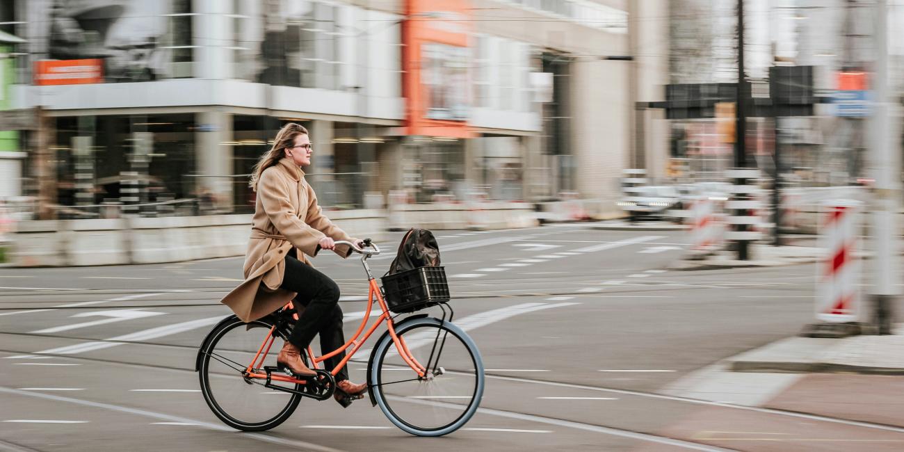 Frau im braunen Mantel fährt tagsüber auf einem schwarzen Fahrrad auf der Straße.