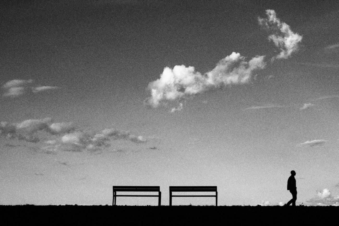 Ein Mensch geht einsam weg von zwei freistehenden Parkbänken