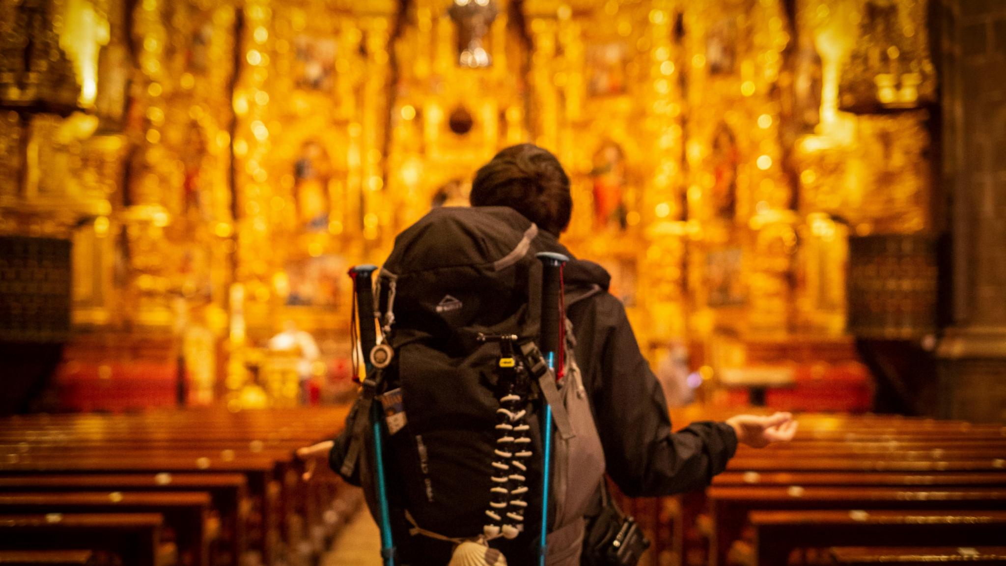 Pilger mit Rucksack, der dem kunstvollen Kirchenaltar zugewandt ist.
