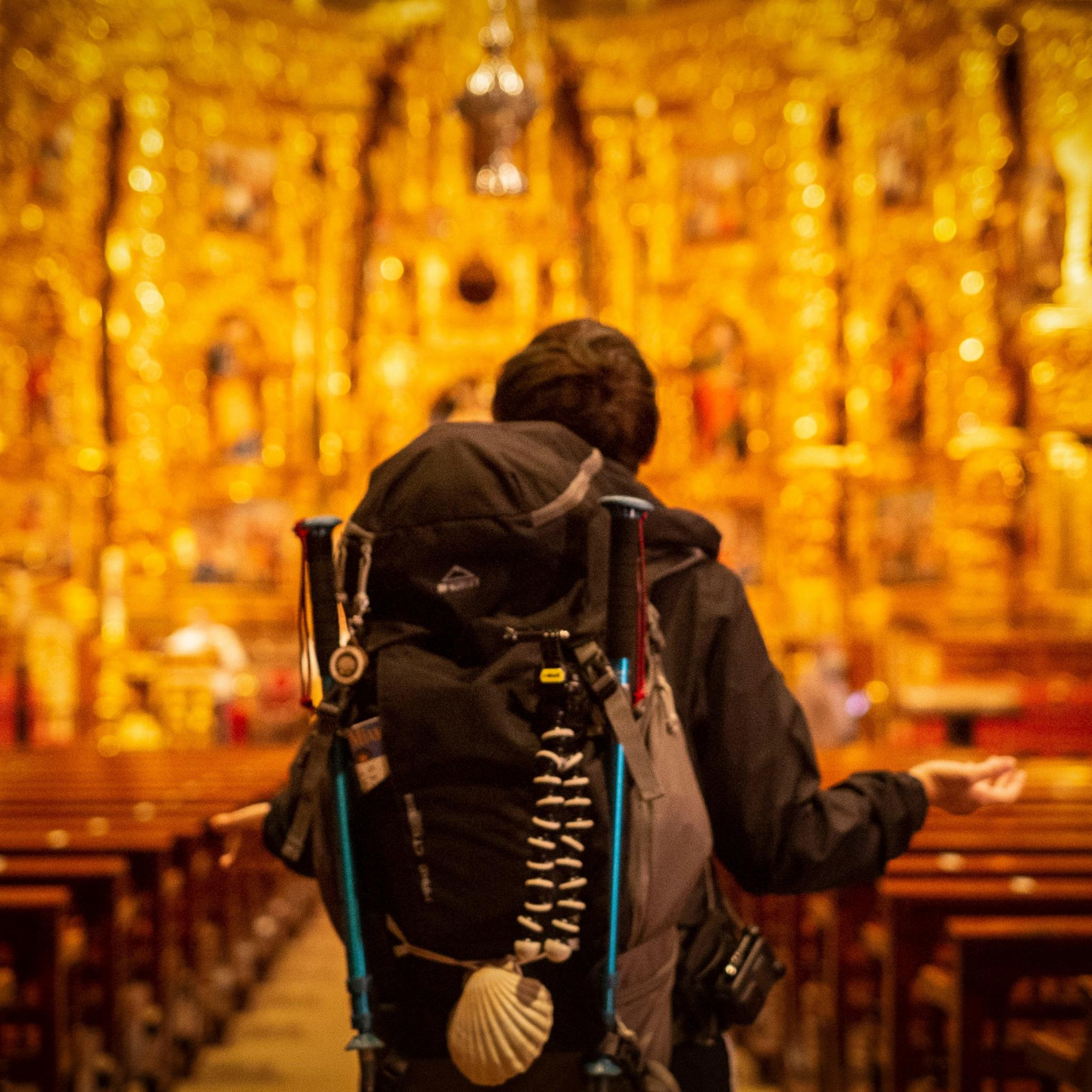 Pilger mit Rucksack, der dem kunstvollen Kirchenaltar zugewandt ist.