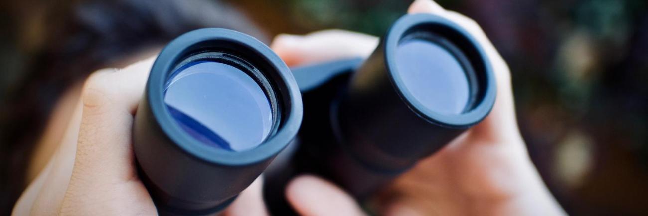 Ein Mensch schaut durch ein Fernglas nach oben.