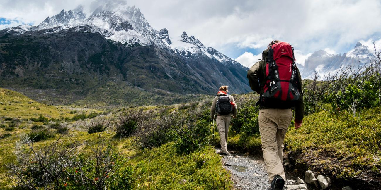 Zwei Personen zu Fuß in Richtung schneebedeckter Berge.