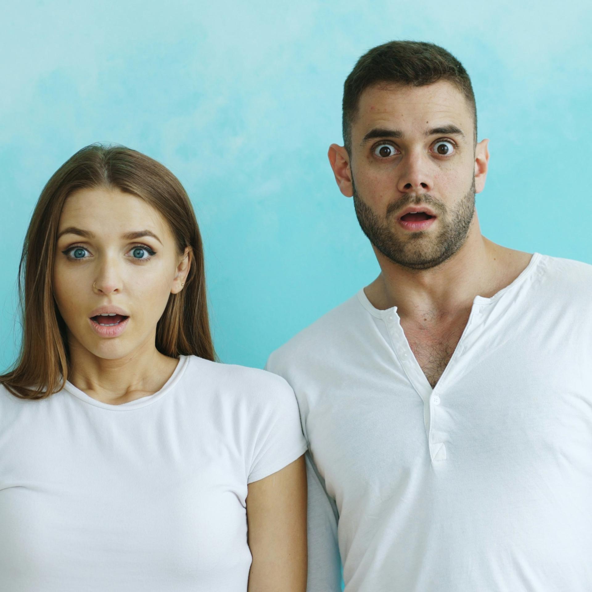 Paar mit schockiertem Gesichtsausdruck vor blauem Hintergrund.