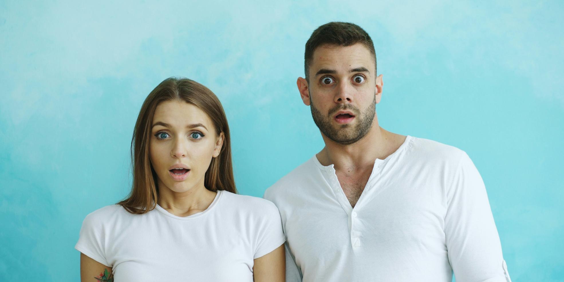 Paar mit schockiertem Gesichtsausdruck vor blauem Hintergrund.