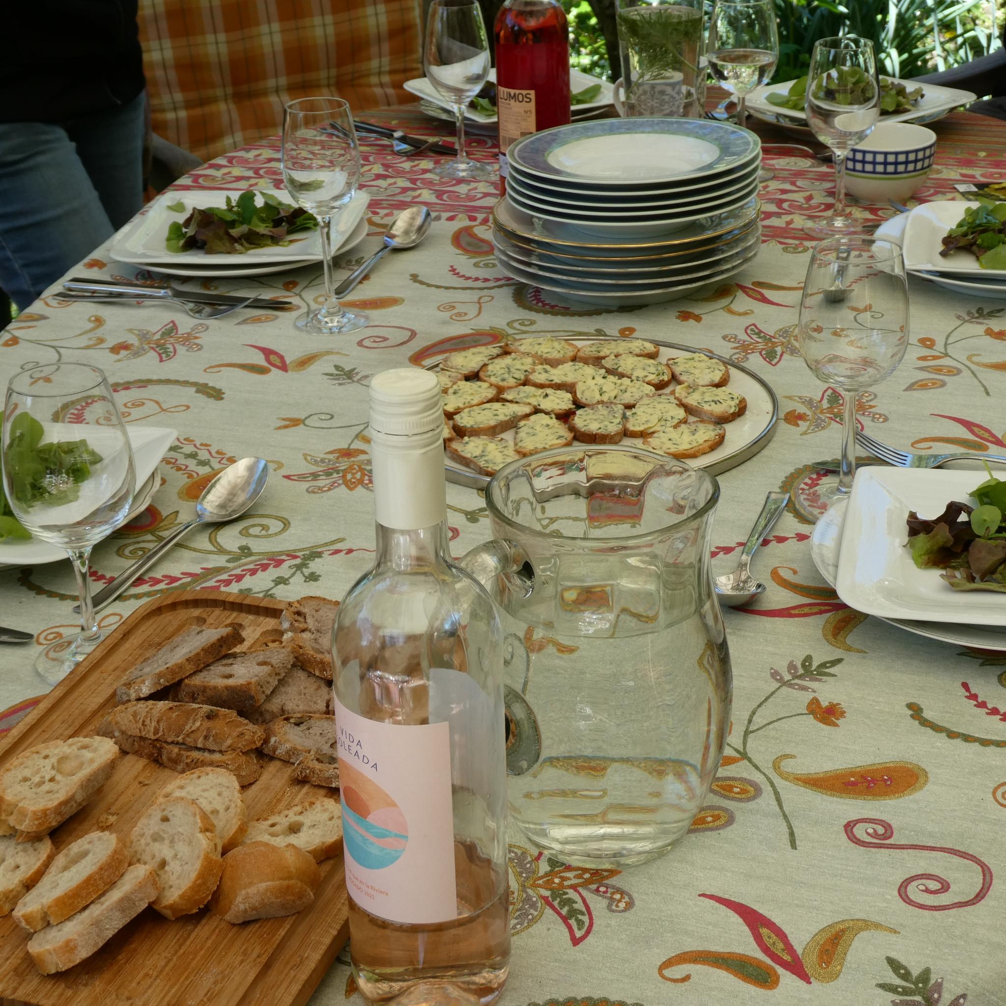 Gartentisch mit Salattellern, Baguette, Wasser und Wein