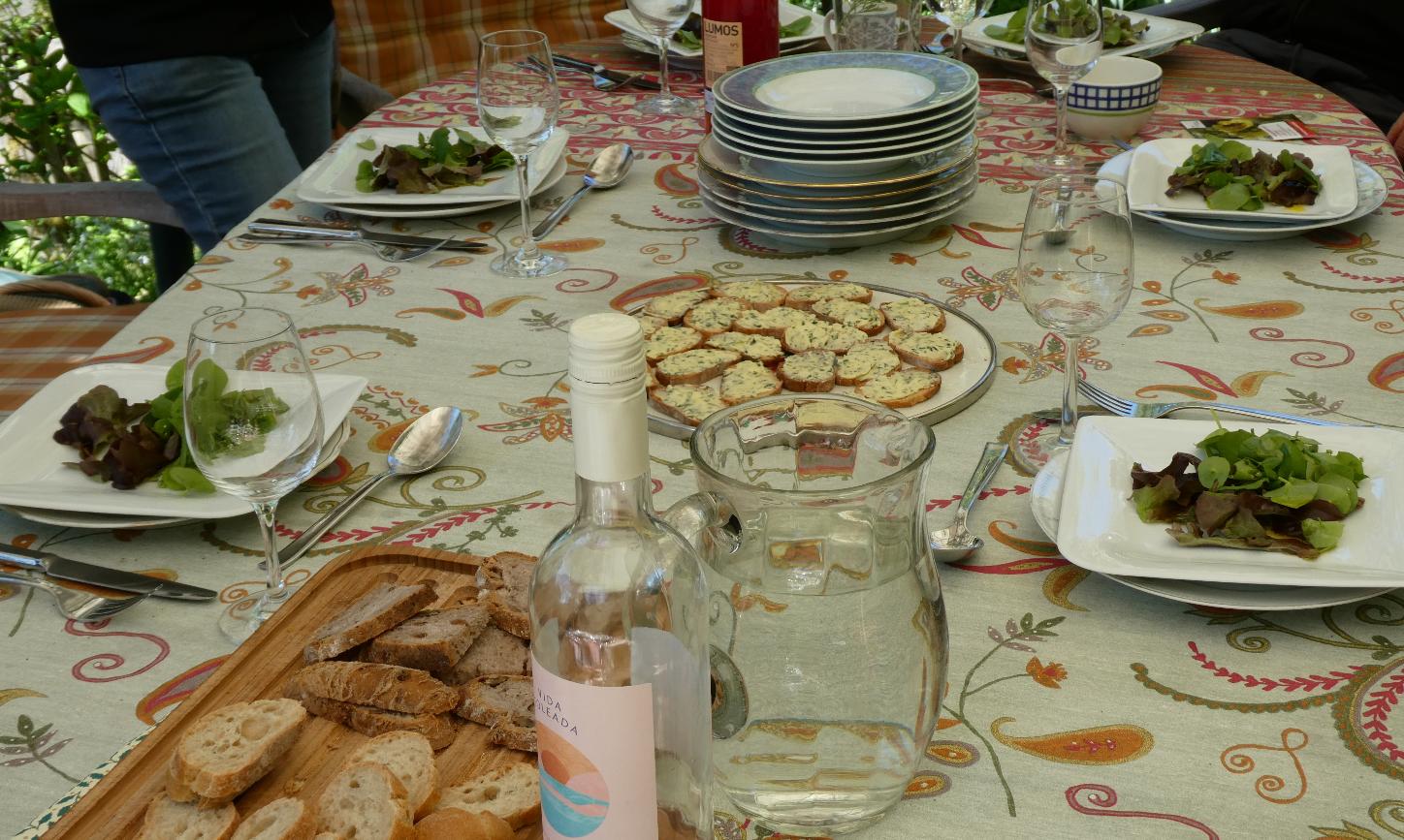 Gartentisch mit Salattellern, Baguette, Wasser und Wein