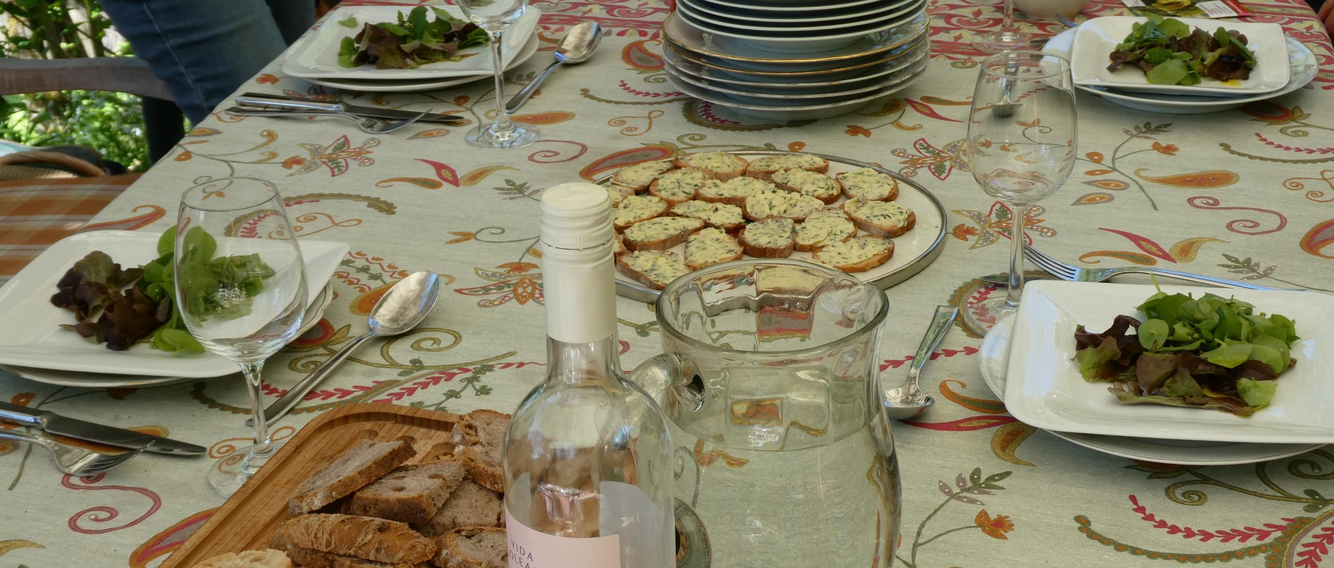 Gartentisch mit Salattellern, Baguette, Wasser und Wein