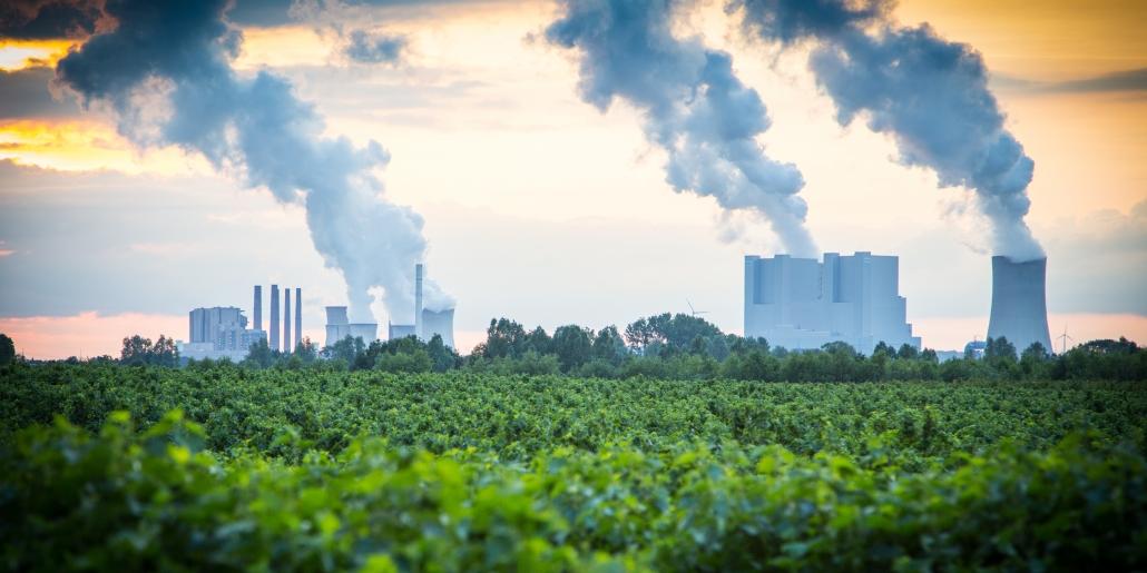 Rauchende Industrieschlote hinter grüner Waldlandschaft