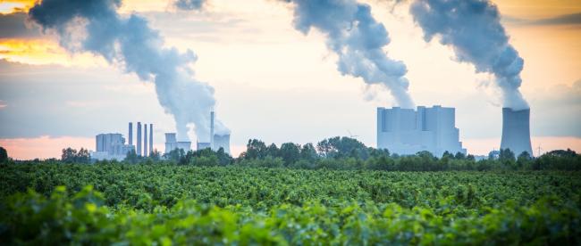 Rauchende Industrieschlote hinter grüner Waldlandschaft