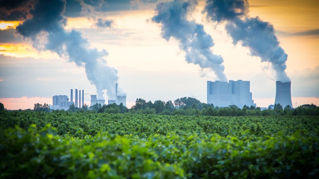 Rauchende Industrieschlote hinter grüner Waldlandschaft