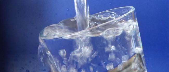 Man sieht, wie ein Wasserstrahl in ein Glas läuft