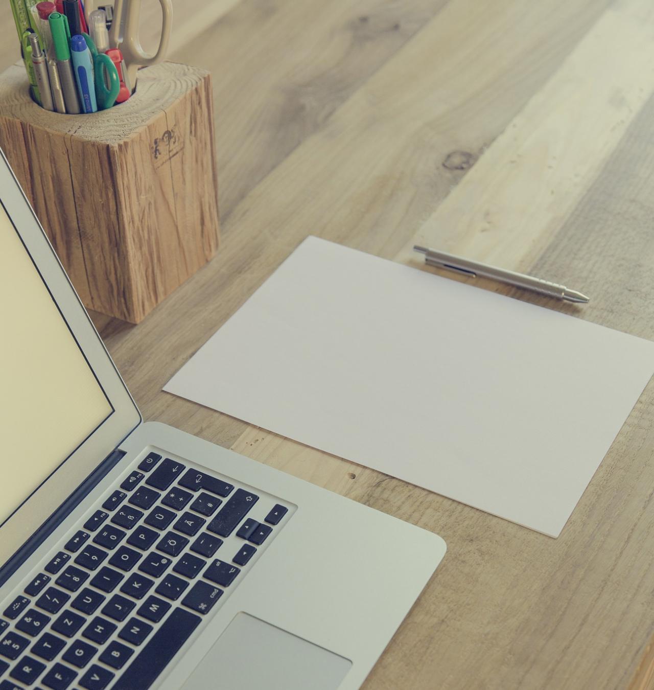 Schreibtisch mit Laptop, Stifteständer, einem Blatt Papier und einem Stift