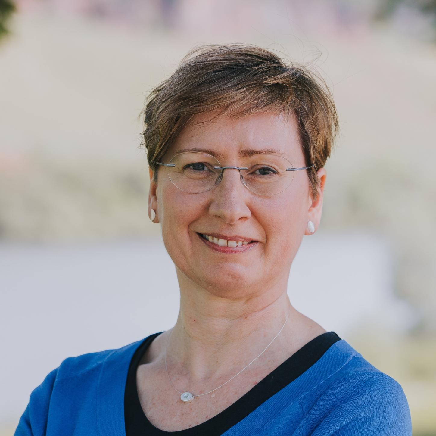 Eine Frau mit Brille und kurzen Haaren lächelt in die Kamera.