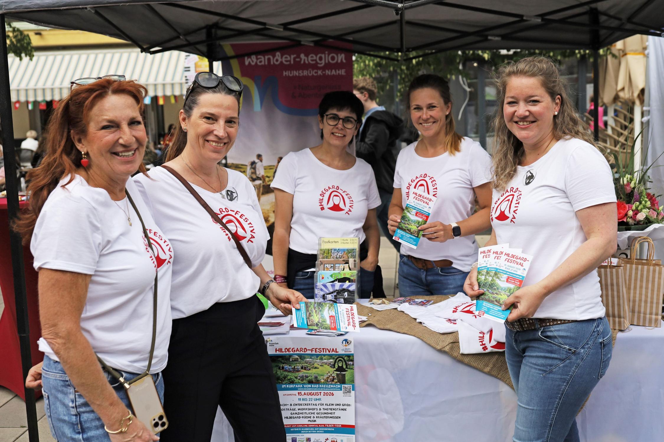 5 Frauen mit T-Shirts (Aufschrift #Hildegard-Festival) stehen am Infostand