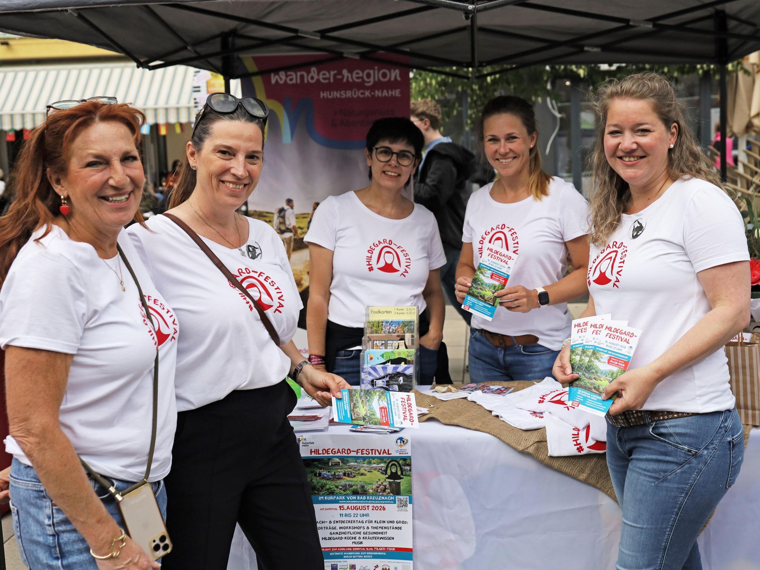 5 Frauen mit T-Shirts (Aufschrift #Hildegard-Festival) stehen am Infostand
