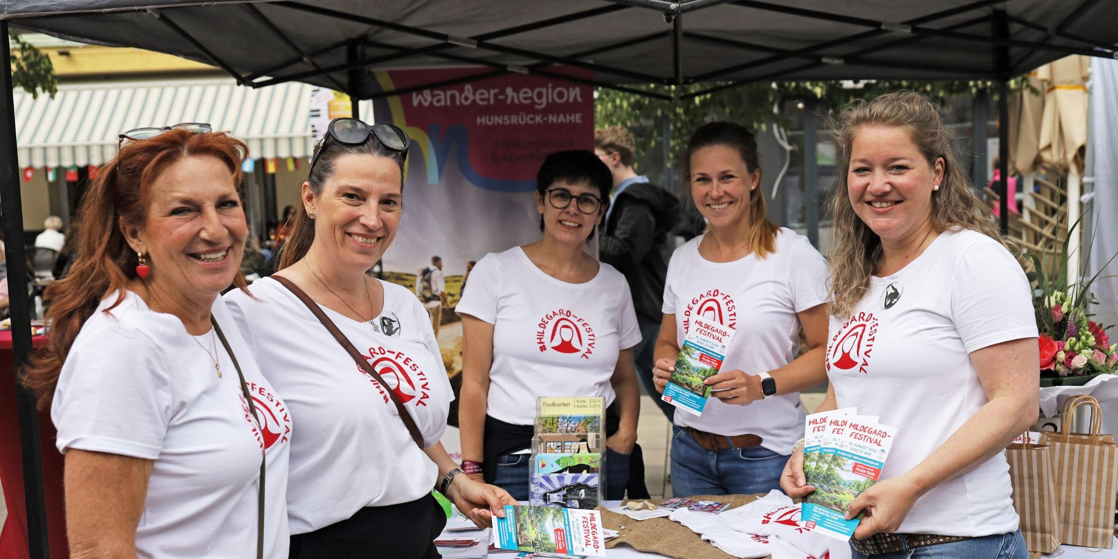 5 Frauen mit T-Shirts (Aufschrift #Hildegard-Festival) stehen am Infostand