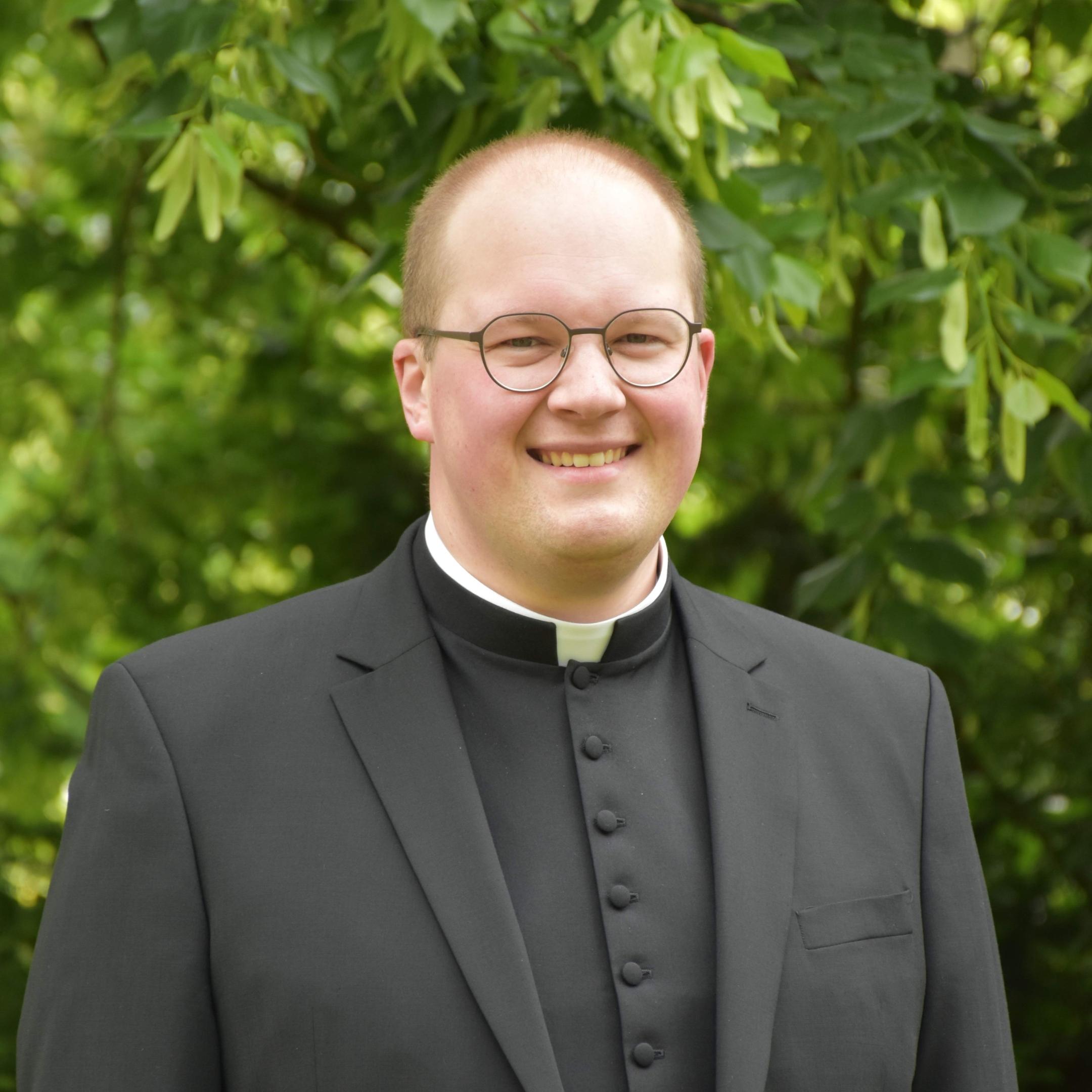 Man sieht Heiko Reiner Gaub im Anzug und Priestercollar. Er trägt eine Brille und lächelt in die Kamera.