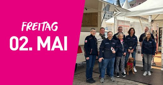 Eine Gruppe der Malteser steht vor einem Infozelt. Links im Bild steht auf pinkfarbenem Hintergrund Freitag zweiter Mai