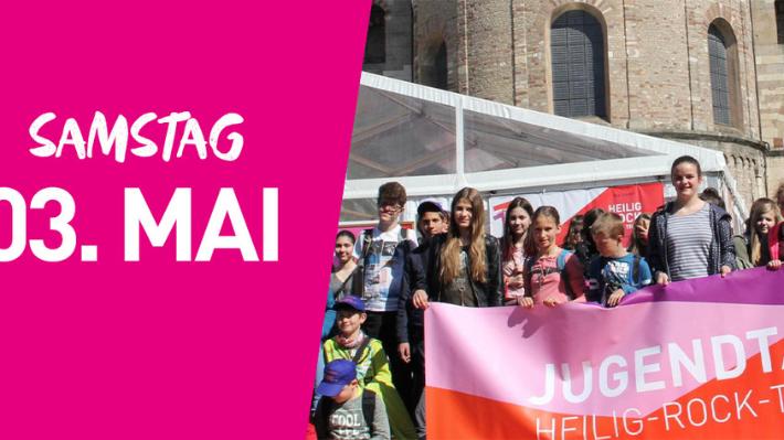 Eine Gruppe junger Menschen steht mit einem großen Banner vor dem Trierer Dom. Auf dem Banner steht Jugendtag. Links im Bild steht auf pinkfarbenem Hintergrund Samstag dritter Mai