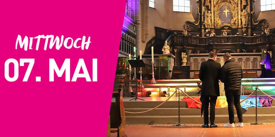 Zwei Menschen stehen in einer Kirche, die Treppe ist bunt beleuchtet, links im Bild steht auf pinkfarbenem Hintergrund Mittwoch siebter Mai