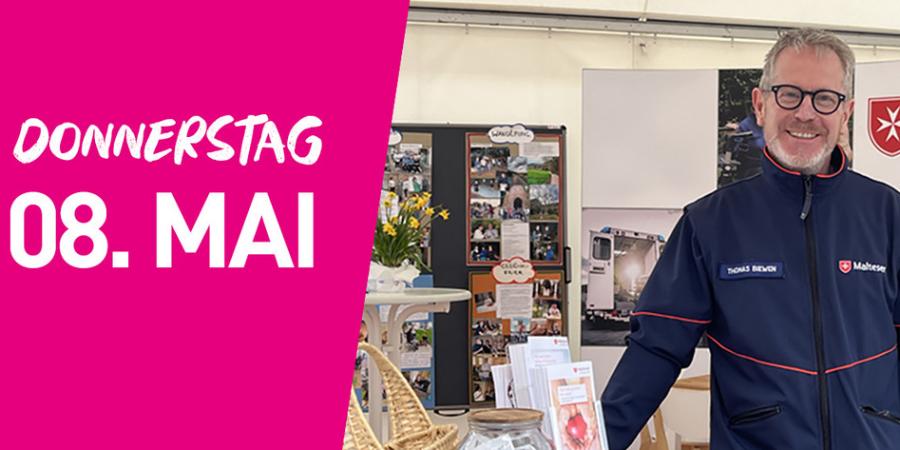 Ein Mann in einer Uniform der Malteser steht am Stand dieser. Auf der rechten Seite steht auf pinkfarbenem Hintergrund Donnerstag achter Mai