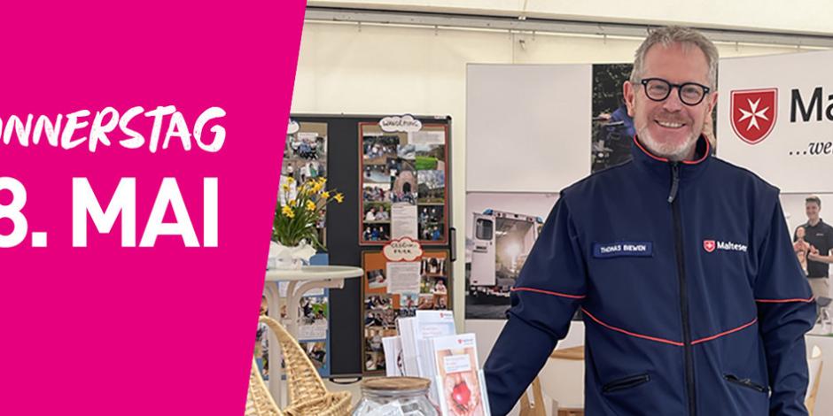 Ein Mann in einer Uniform der Malteser steht am Stand dieser. Auf der rechten Seite steht auf pinkfarbenem Hintergrund Donnerstag achter Mai